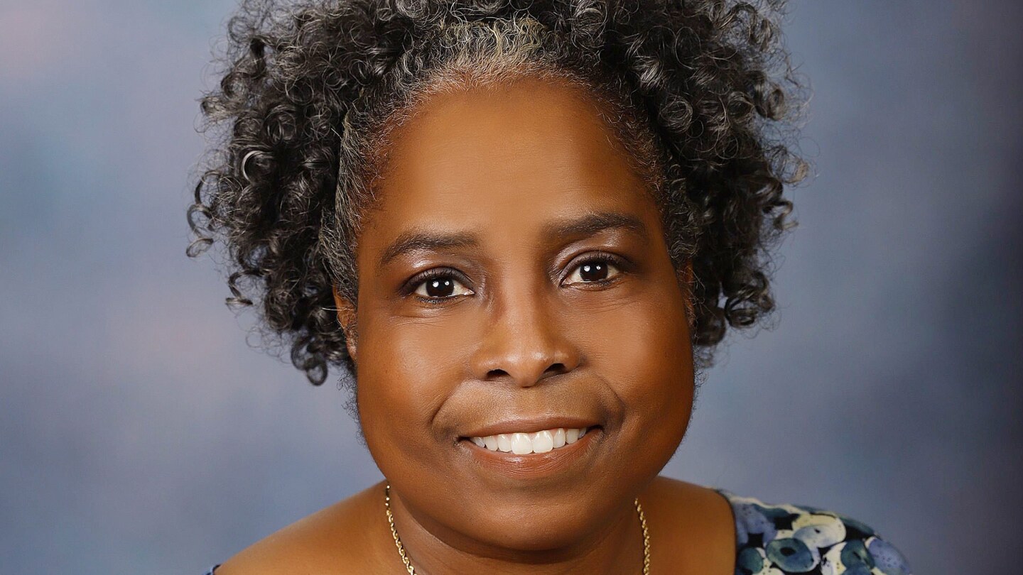 Rev. Dr. Phyllis Everstine Hayes-Reams smiles at the camera. She has short, curly grey hair and is wearing a top with blue and white abstract circles on it.