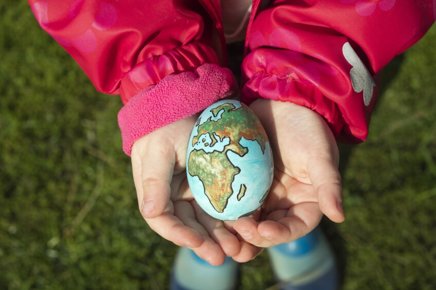 Un niño sostiene un huevo pintado como el planeta Tierra en un día soleado al aire libre.