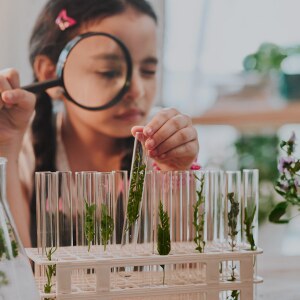 A little girl looks at test tubes through a magnifying glass. iStock