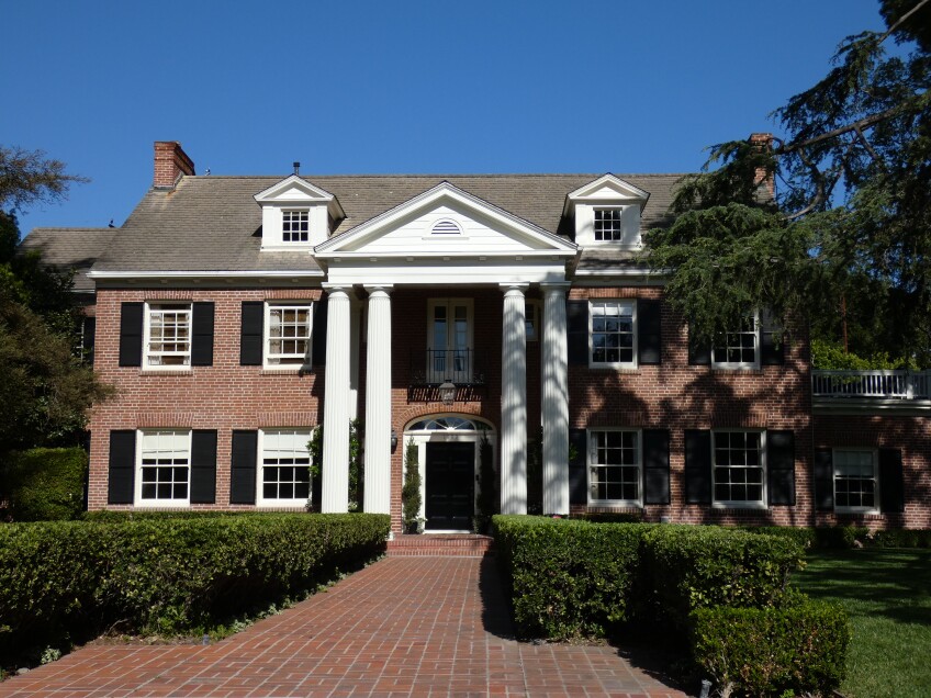 A two story house with a red brick exterior and symmetrical windows on either side of the entrance. The entrance is decorative, with white Greek-like columns on either side of the door. 