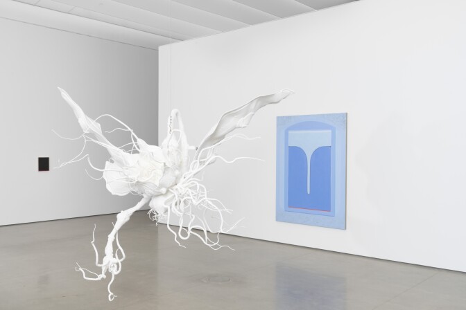 A white sculpture hangs in front of a blue painting in a gallery at OCMA.