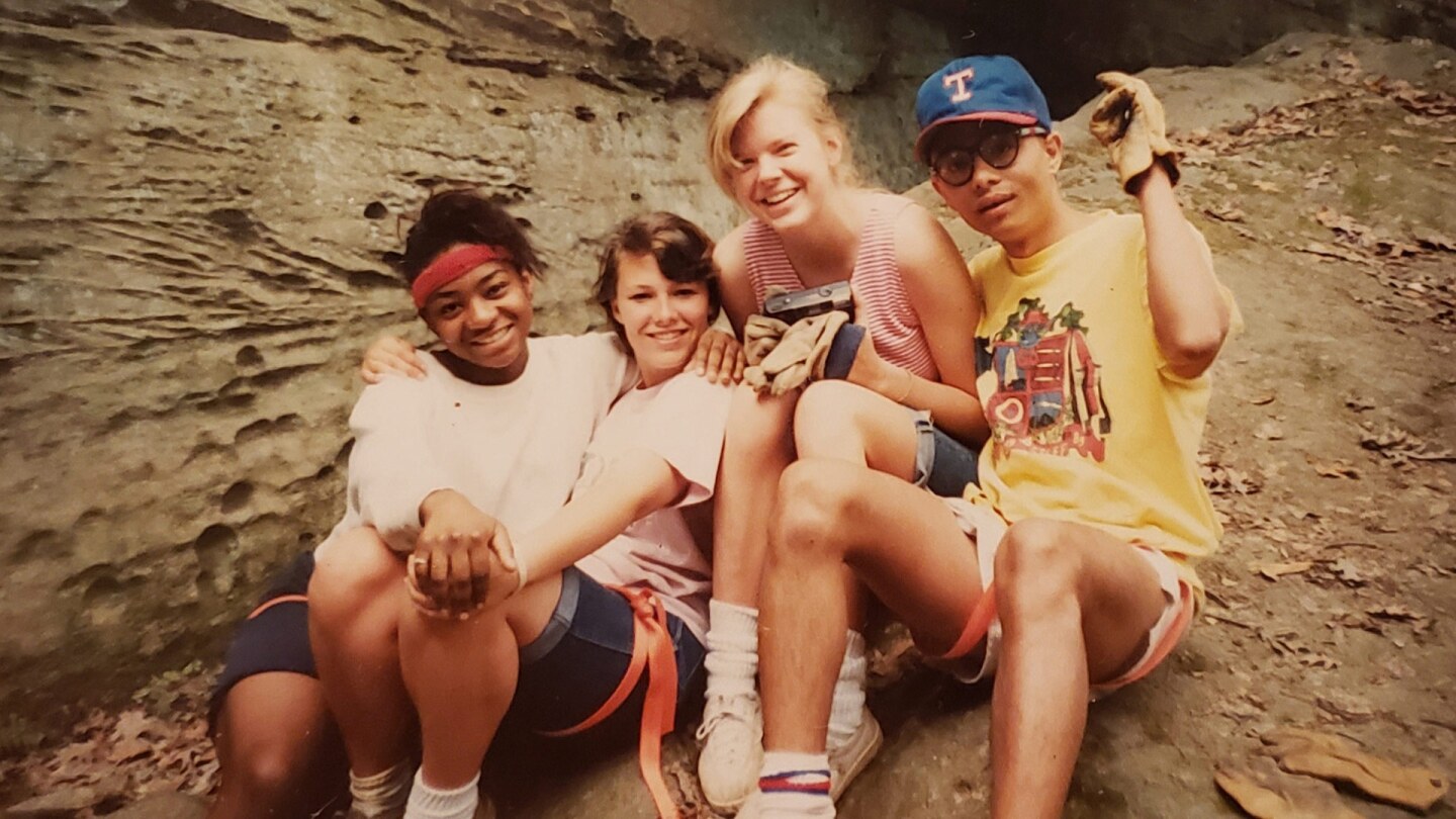 Three young women and a young man sit together on some rocks.