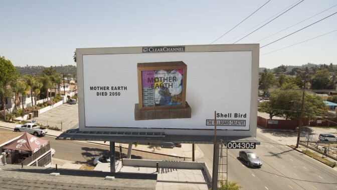 A billboard shows a shadow box with a clear, see-through pane. On the transparent pane are the words "Mother Earth" printed on it. Inside the box are various pieces of trash and plastic. To the left of the box are the words, "Mother Earth died 2050."