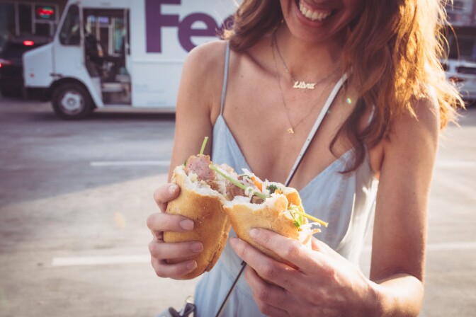 A woman holding and tearing apart a bánh mì sandwich.