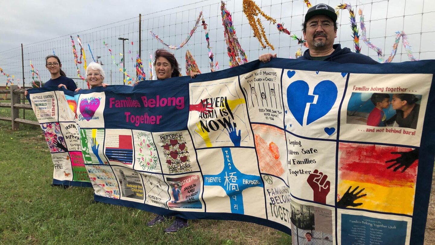 Four people hold a colorful quilt in protest