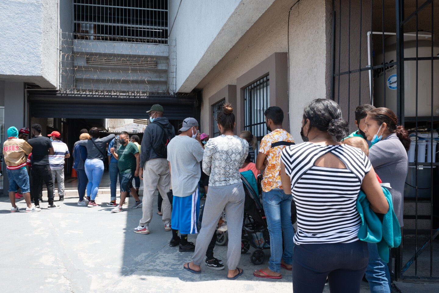 Masked people stand up in a line that snakes around a building.