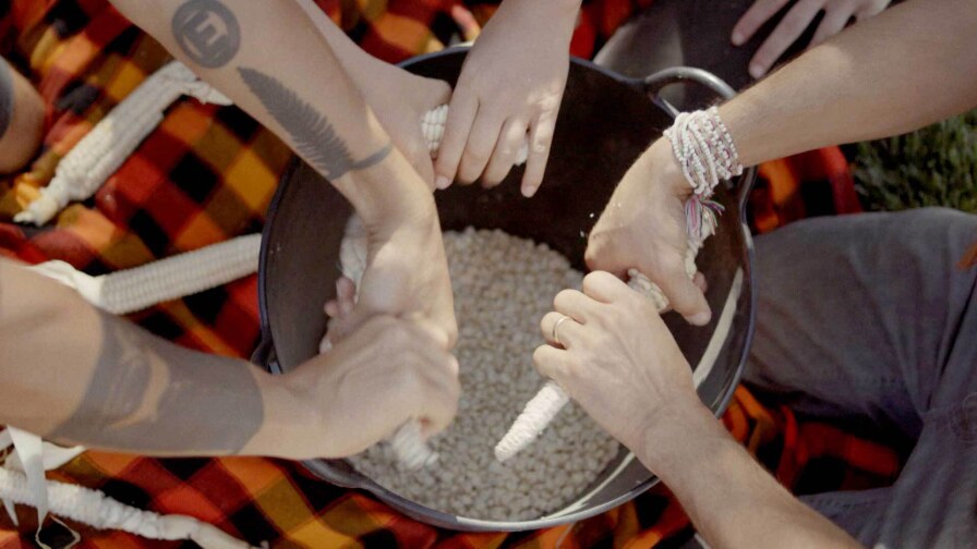 A group at the Cultural Conservancy removes dried grain corn from the cob to preserve the seeds in their seed library. | Still from the "Cultivating Native Foodways with the Cultural Conservancy" episode of "Tending Nature."