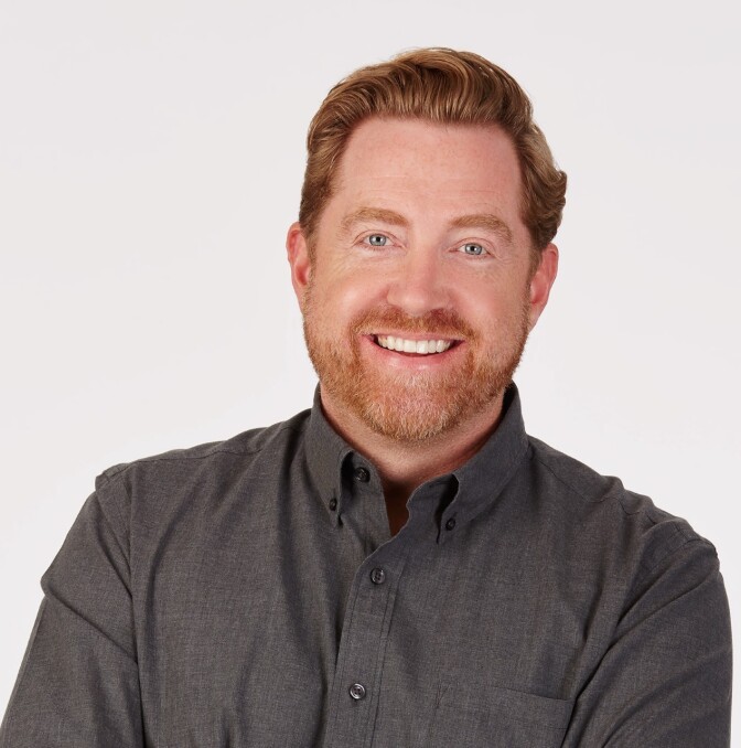 A man with a beard and a button shirt smiles at the camera