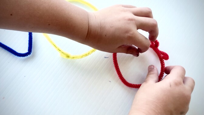Closeup of a small child's hands as they shape craft pipe cleaners into different shapes like triangles and circles.