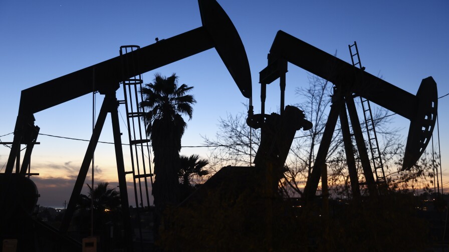An oil pump jack (L) operates as another (R) stands idle as the sun sets in the background.