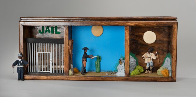 A three-panel miniature diorama with wooden frames depicts three scenes in the life of U.S. Marshall Bass Reeves. The first panel depicts a Black man in a sheriff uniform standing outside of a jail cell. The second panel depicts a Black man wearing a cowboy hat and a gun holster around the waist pointing a gun at a glass bottle. The third panel depicts a Black man in tattered clothes in the middle of a desert landscape with the moon behind him.