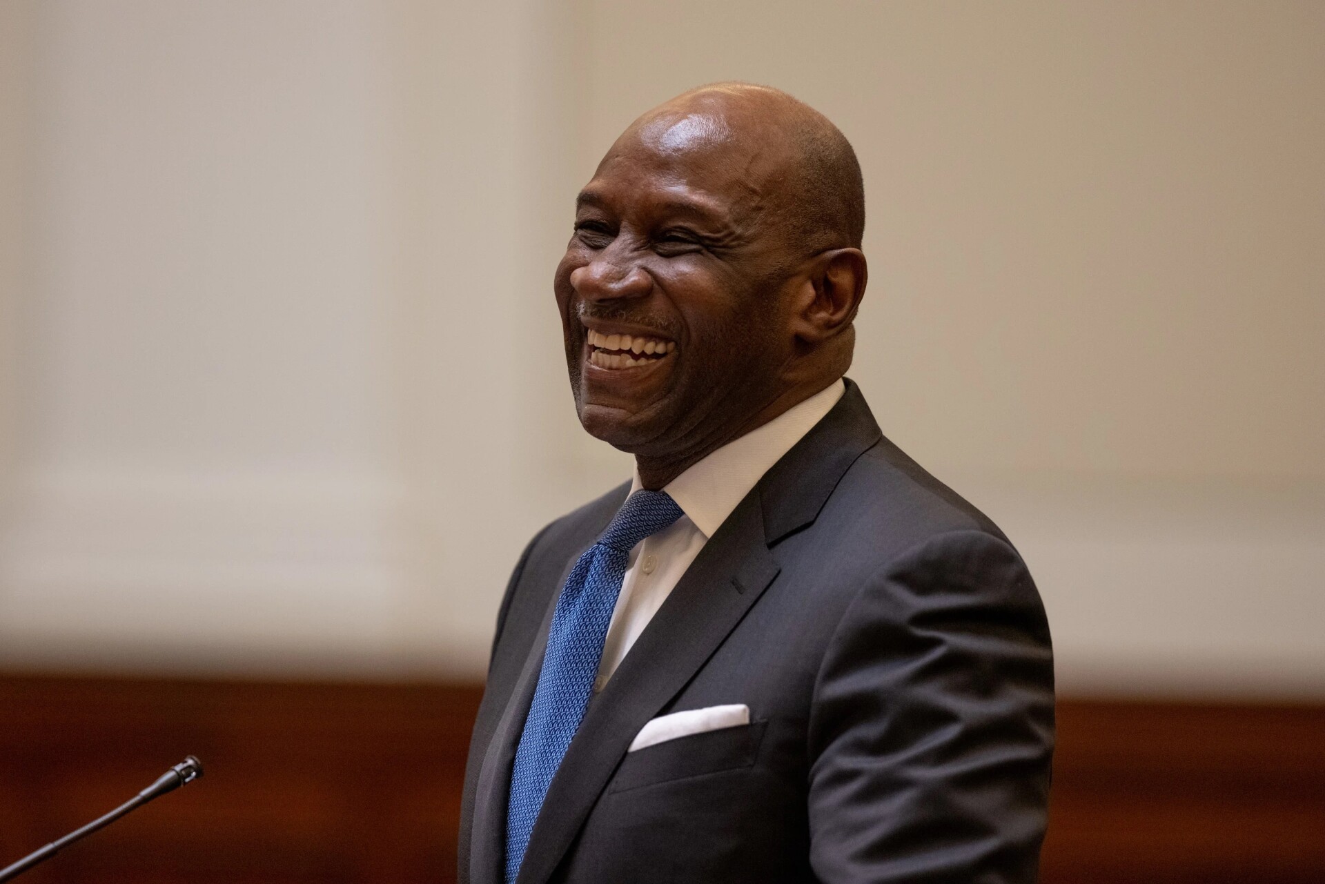 Mark Jenkins, dressed in a suit and tie, smiles from behind a microphone in a courtroom