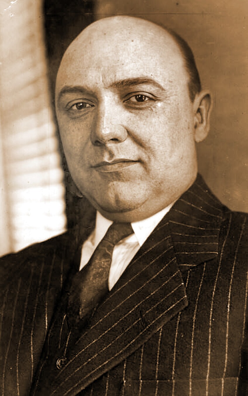 A black and white photo of Sheridan C. Lewis -- a bald middle aged man. The photo is taken from the chest up. He is wearing a pin-striped suit jacket and tie.