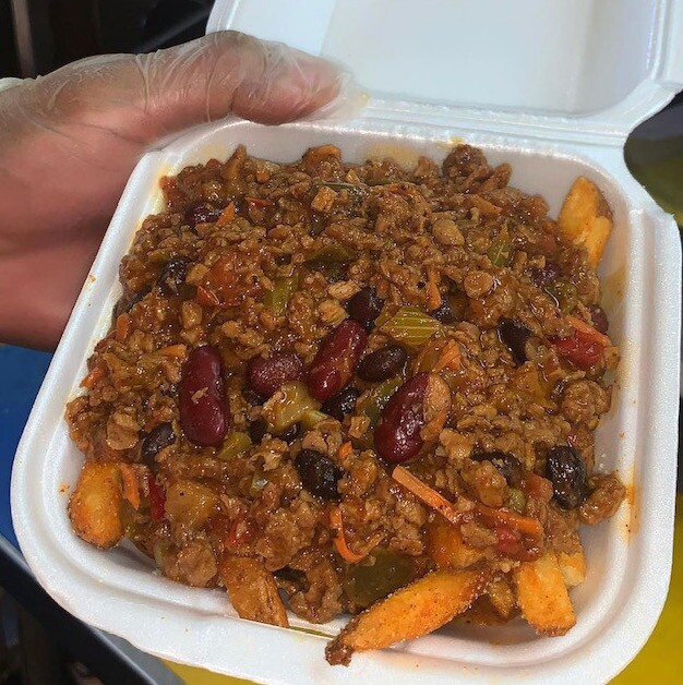 Seasoned fries topped with a vegan chili sit in a styrofoam container.