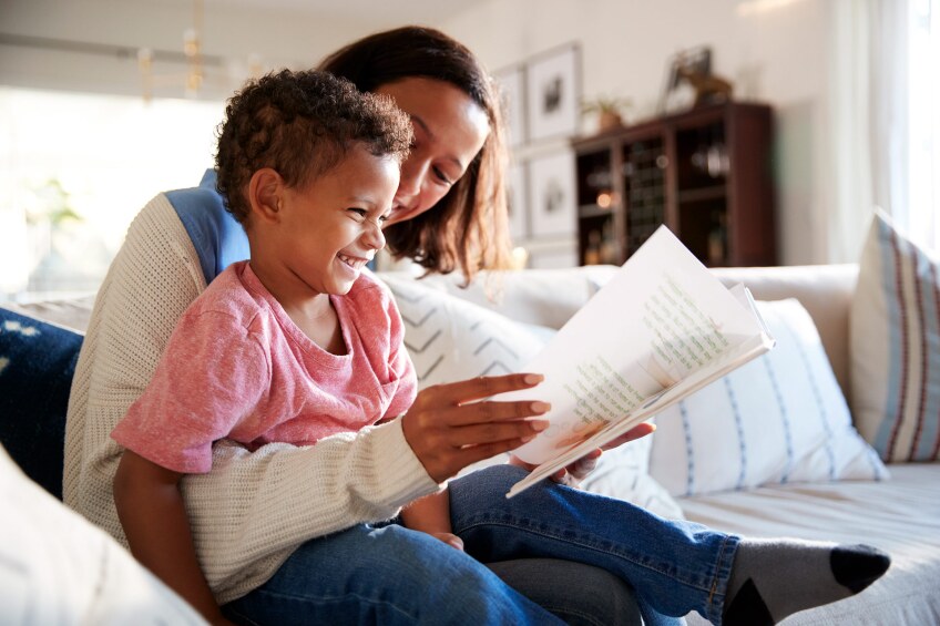 A woman and a little boy read together on a couch