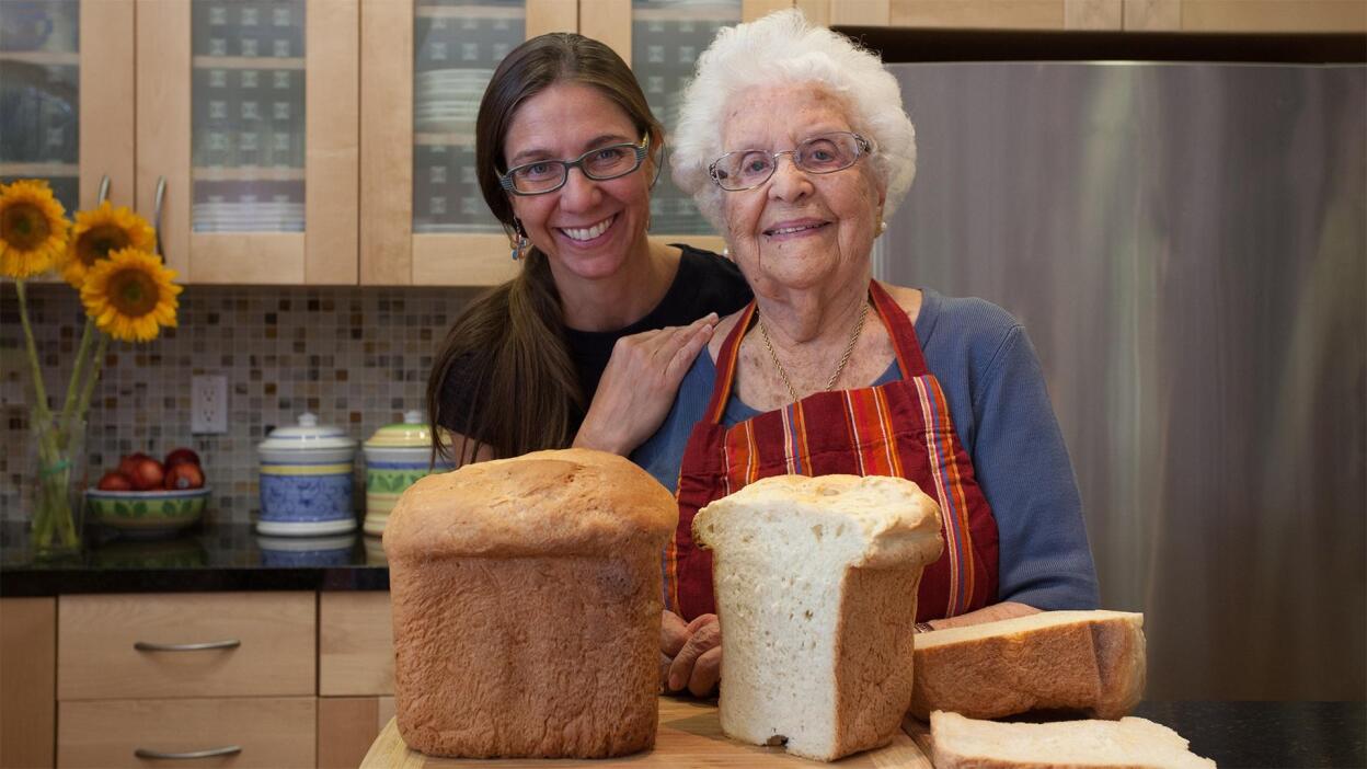 Two people standing behind loaves of bread in a kitchen pose for the camera.
