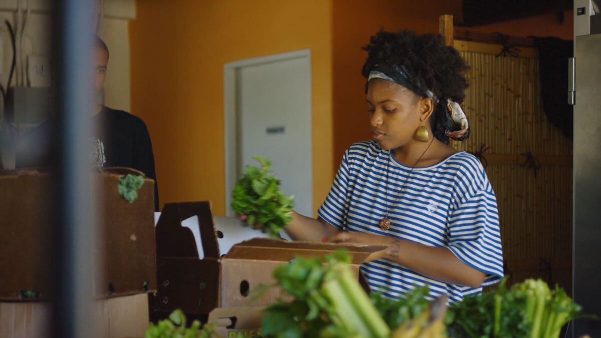 Olympia Auset arranging produce | Still from "Broken Bread" Access