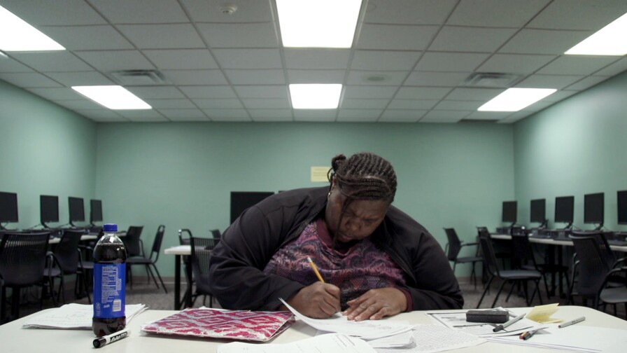 Night school student Melissa intently writes on a piece of paper in an empty computer lab. | From "Night School"