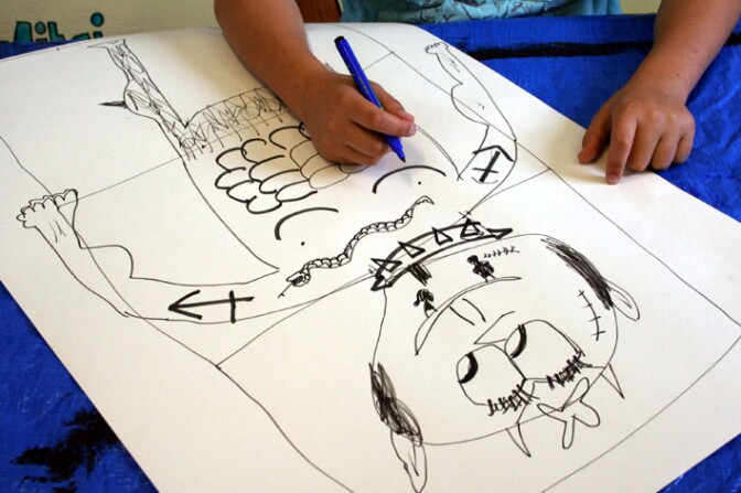 A child helps draw a traditional Exquisite Corpse activity
