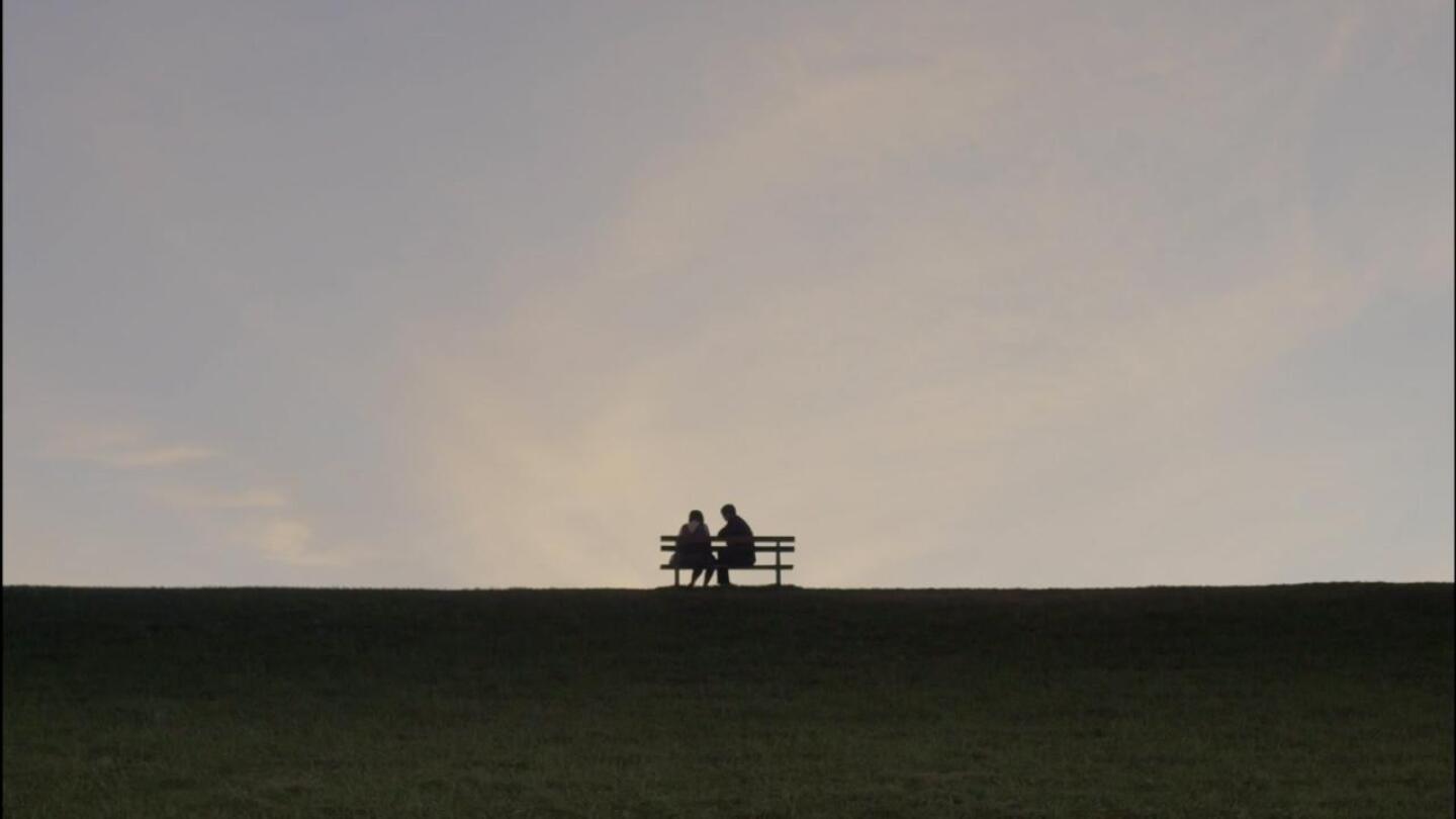 Silhouette of two people sitting on a bench in the distance.