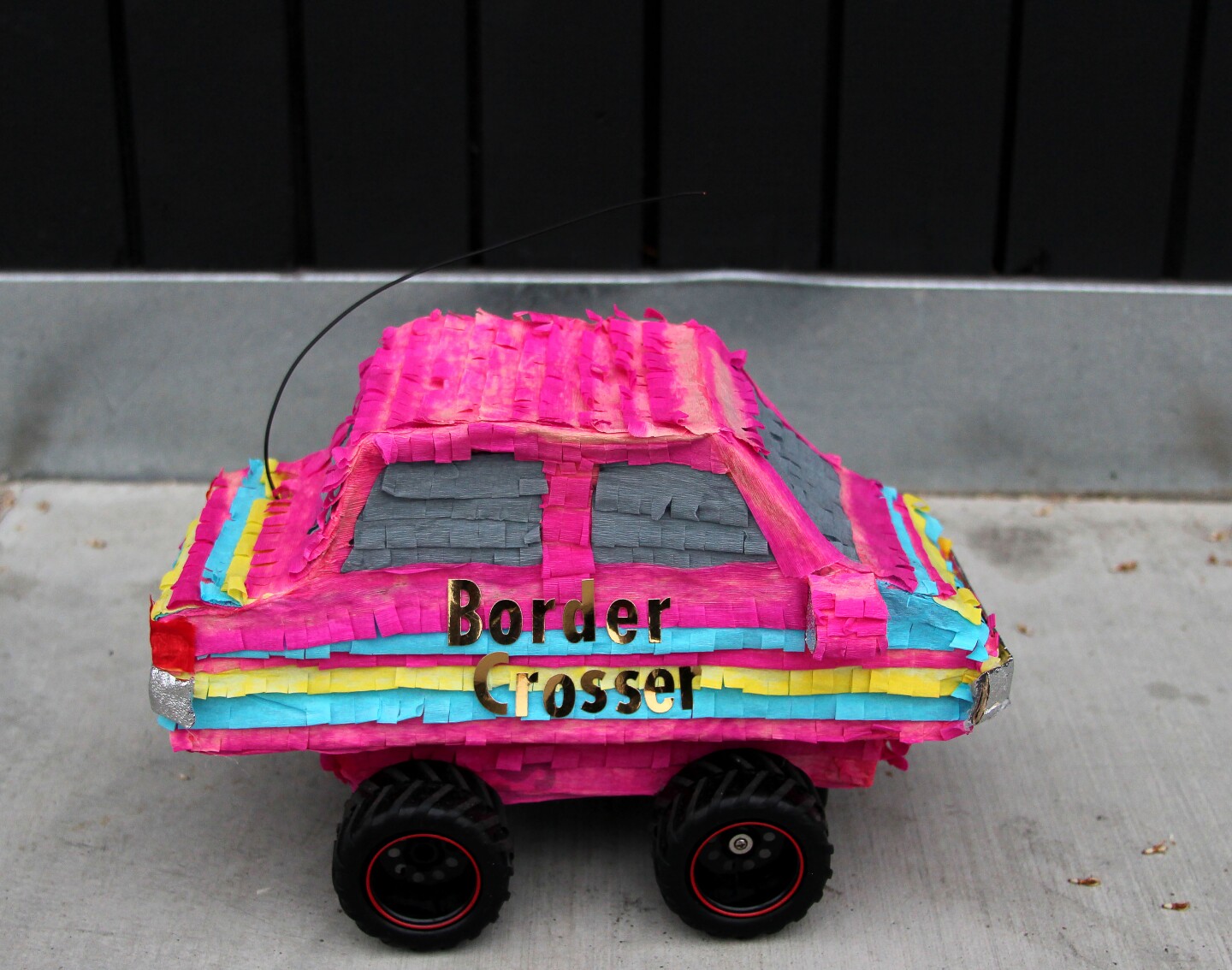 A colorful pink car striped with yellow and blue is made out of crepe paper and reads "Border Crosser."