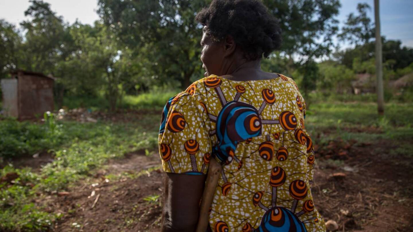 Matina, 67, stands in front of the plants she is growing to feed the seven children she supports. She is skipping her antiretroviral medication because it hurts her stomach to take it without food. Gulu, Uganda. | Thomson Reuters Foundation/Sally Hayden