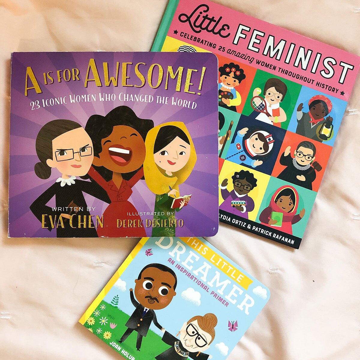 Three colorful children's book featuring historic women and/or Justice Ruth Bader Ginsburg lie on a cream colored sheet.