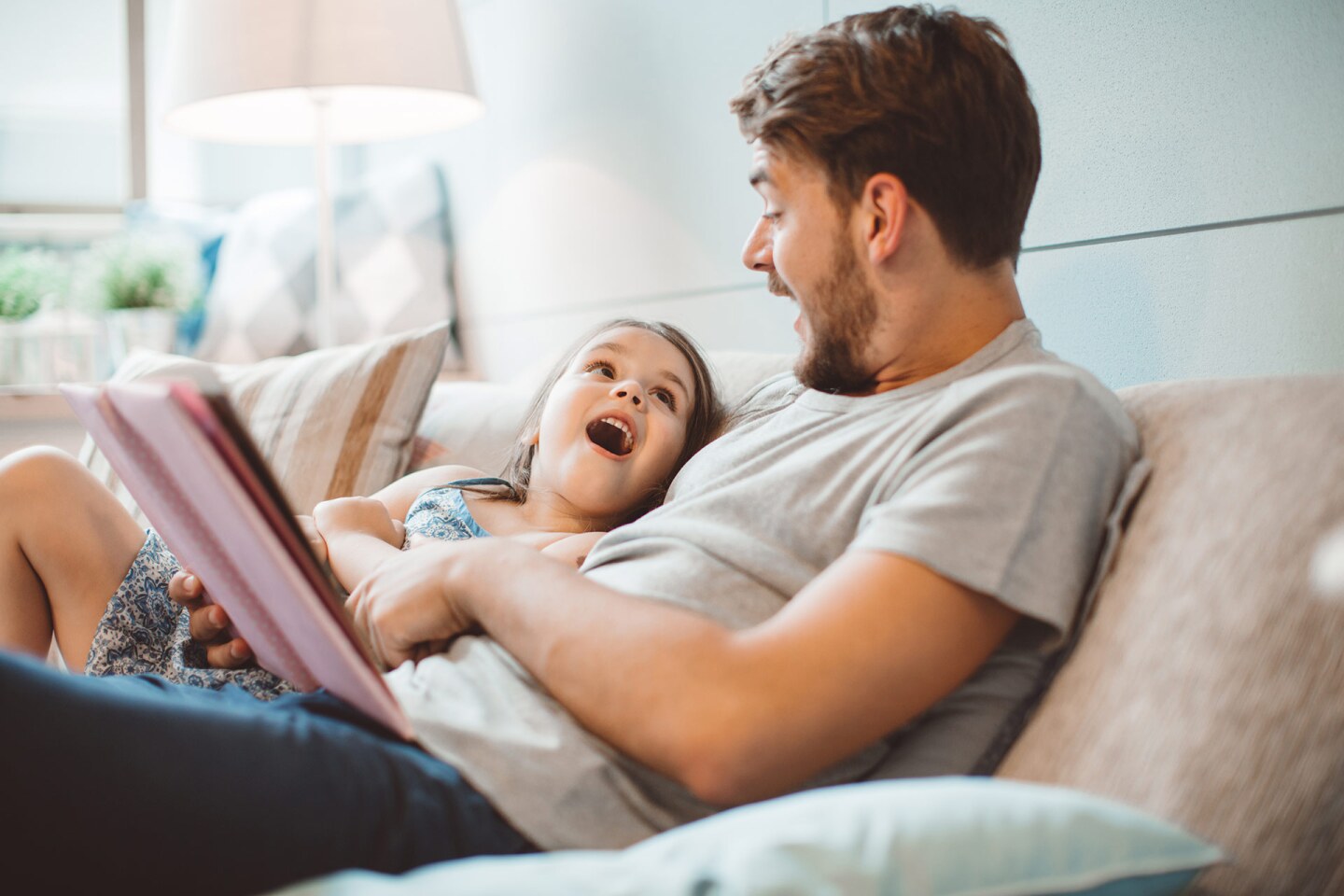 A man an a small girl read together on a couch as they gasp in wonder together.