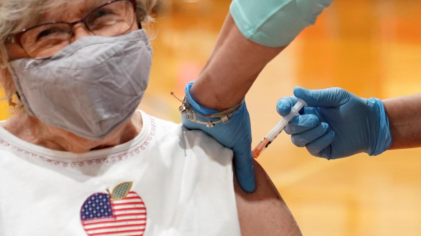 A woman wearing a mask receives a vaccine shot in her arm from a healthcare worker.