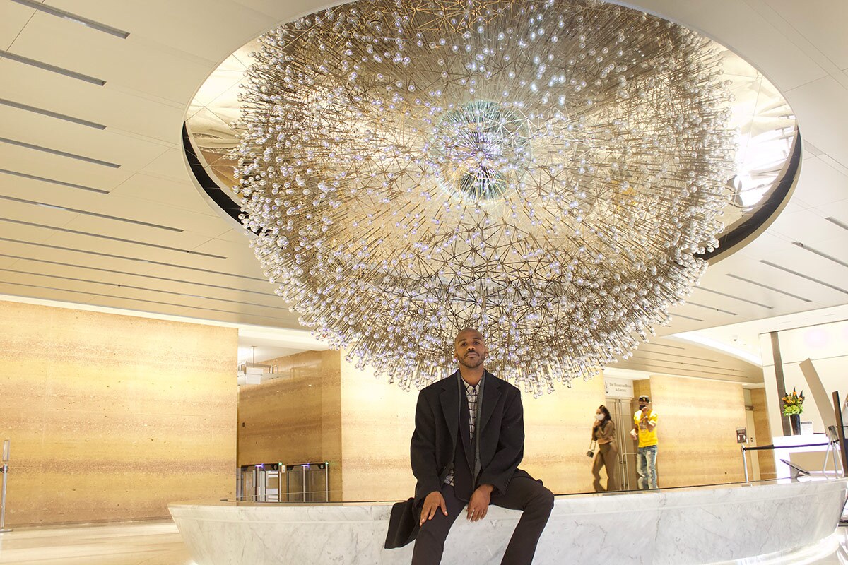 A young person sits below a crystal sculpture hanging from the ceiling.