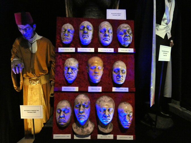 Face molds of horror greats are displayed on a red velvet board. They are organized in three rows and are each face is labeled. A faint blue light lights the faces from below, giving off a spooky aura and feel.