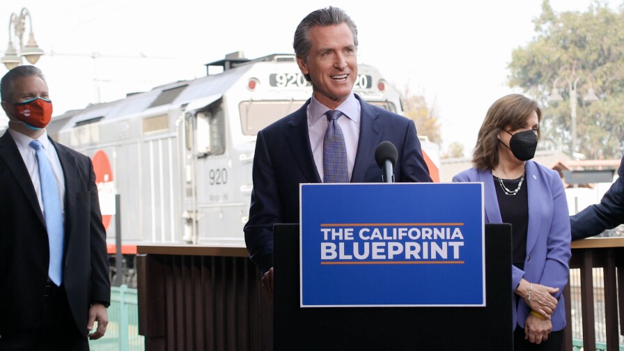 Gov. Gavin Newsom speaks in front of a podium with a sign reading "the California Blueprint".