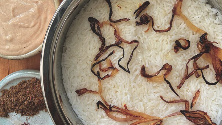 A small, brown pot of biryani. Next to it is a small bowl with brown spices.