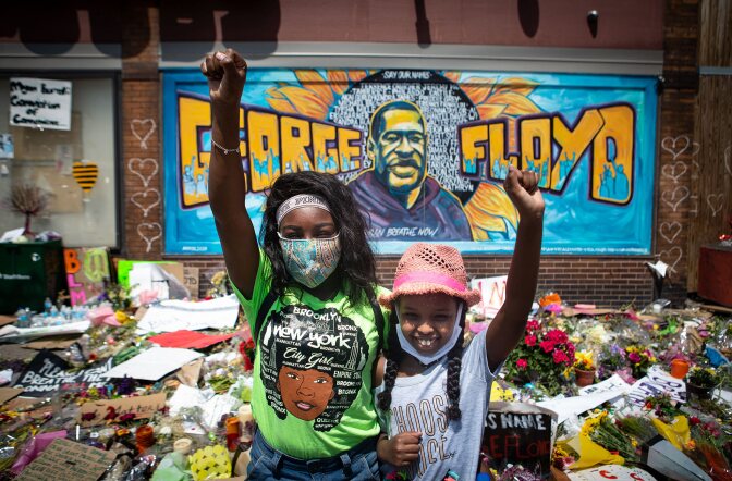 Two girls with fist raised pay their respects at the makeshift memorial for George Floyd