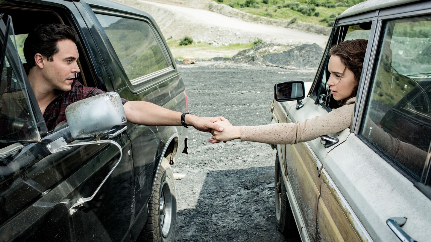 A man and woman sitting different cars hold hands through the windows.