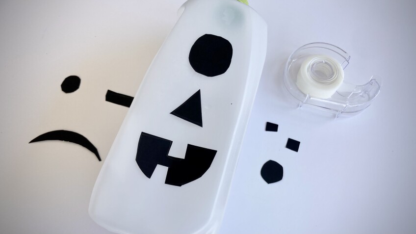 a jack-o'-lantern face made out of construction paper is taped on an empty plastic milk jug