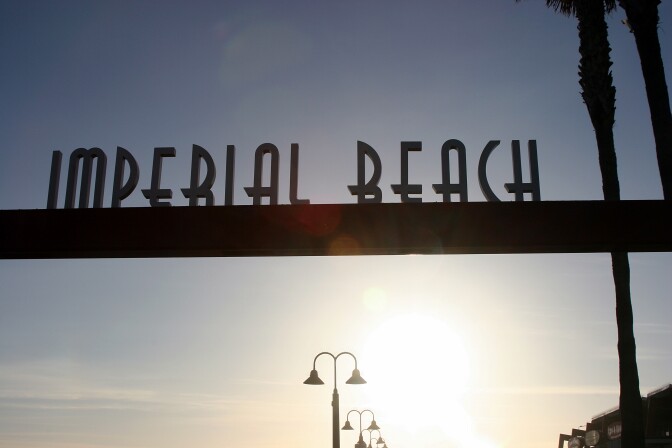 Sign reading "Imperial Beach" with sunset in the background.
