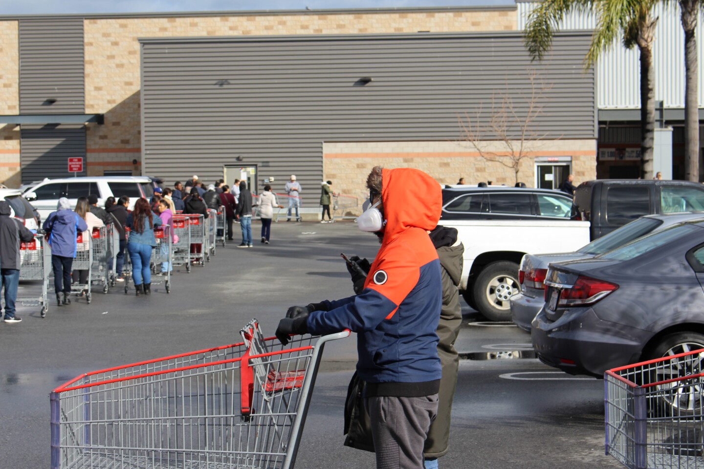 Man in orange sweatshirt with mask with a shopping cart, outside of Costco on March 15th, 2020