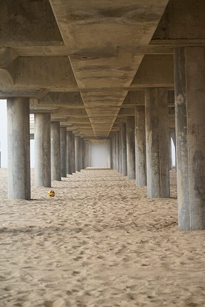 The view of a sandy beach underneath a tall pier. 