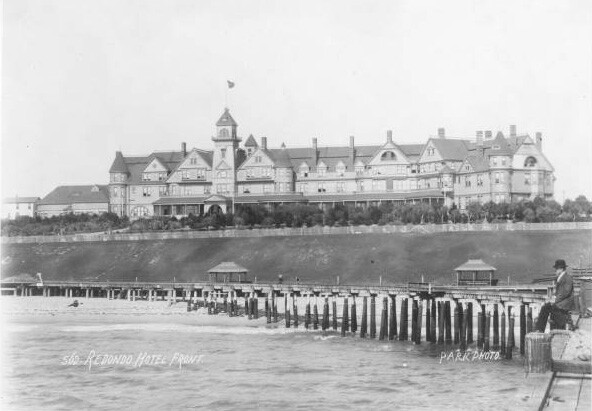 A man sits on a pier in front of the Redondo Hotel on Redondo Beach, 1894. From the South Bay Photograph Collection