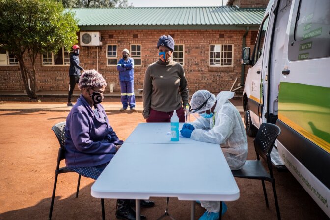 A nurse wearing PPE assess a masked person sitting in front as another masked person looks on. | Thomson Reuters Foundation