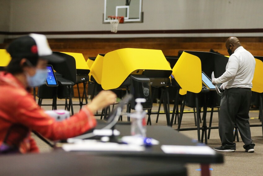 A voter (R) stands at the voting booth as an election worker sits (L) at a Vote Center located at Compton College