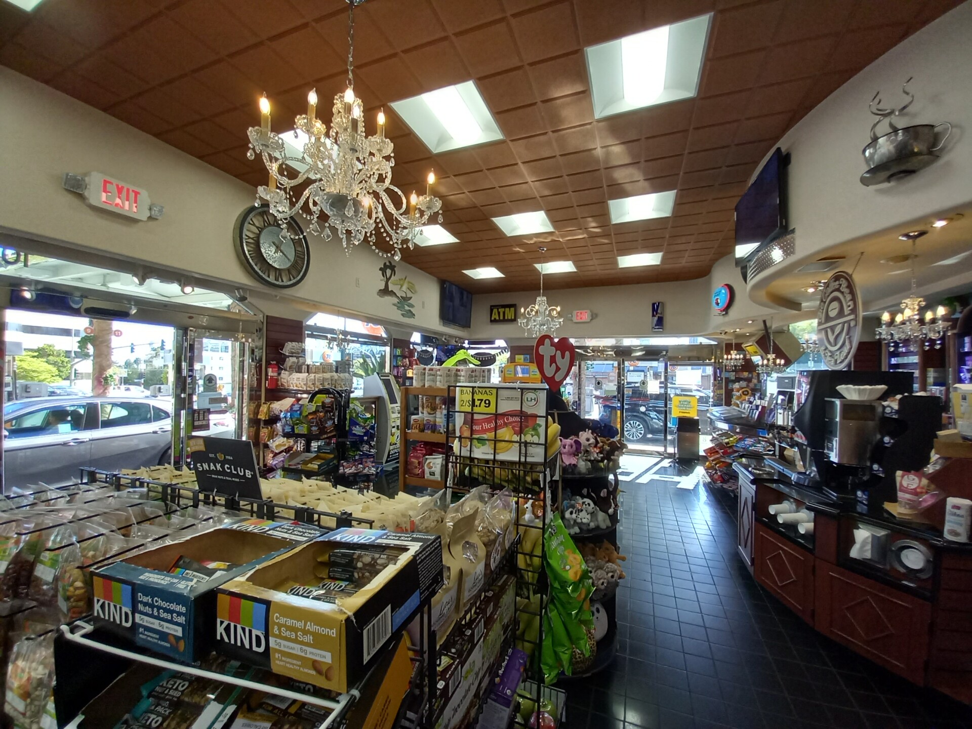The inside of a gas station convenience store. A crystal chandelier hangs from the ceiling above racks filled with miscellaneous snacks from trail mixes and granola bars to cookies and chips.