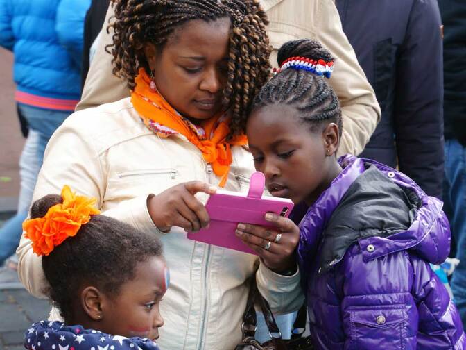 A young girl looks over her caregiver's cell phone.