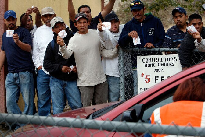 Holding their assigned numbers, day laborers try for the attention of a homeowner looking for gardening help at the day laborer work site.