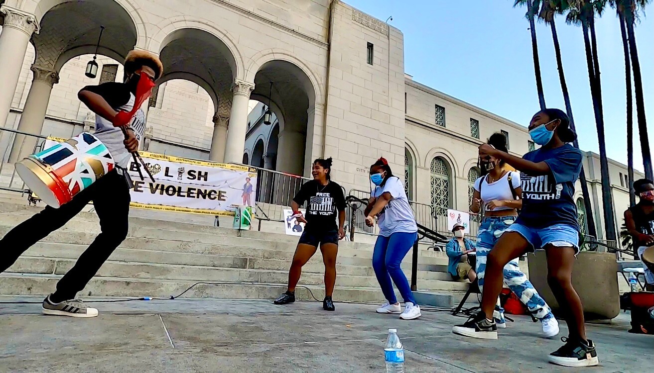 A protestor rallies people as he plays a bucket turned drum.