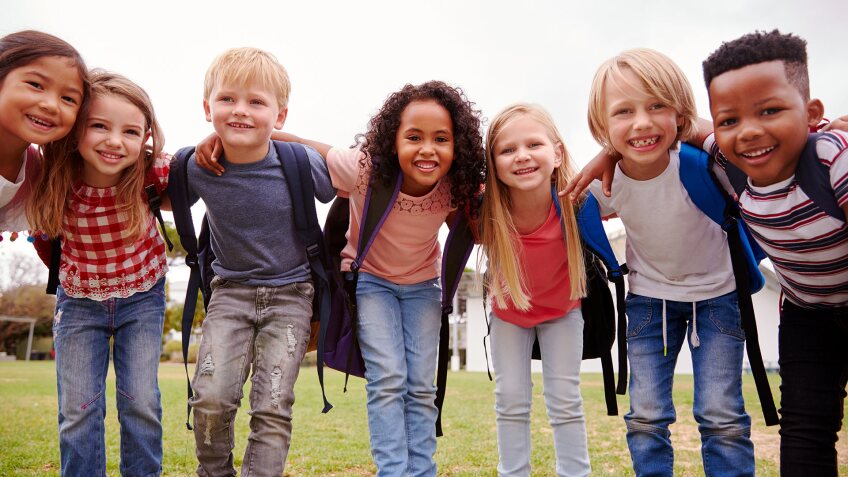 Seven small children of different skin tones huddle together and smile at the camera. iStock