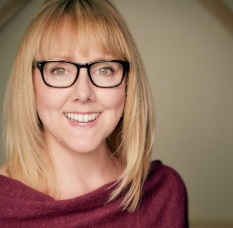A woman with black glasses smiles at the camera