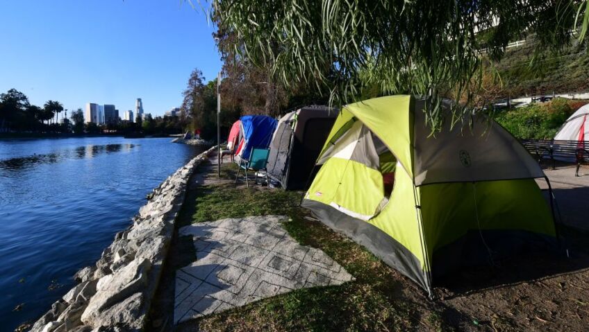 Three camping tents are lined up next to each other in front of a body of water with the Los Angeles skyline in the background.