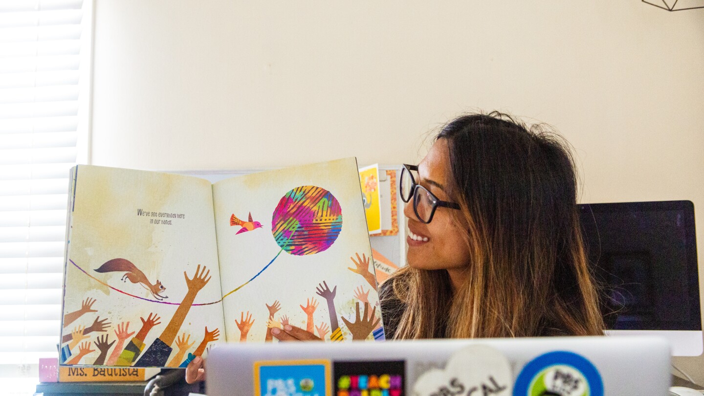 Teacher Shelly Bautista reads aloud in front of a laptop.